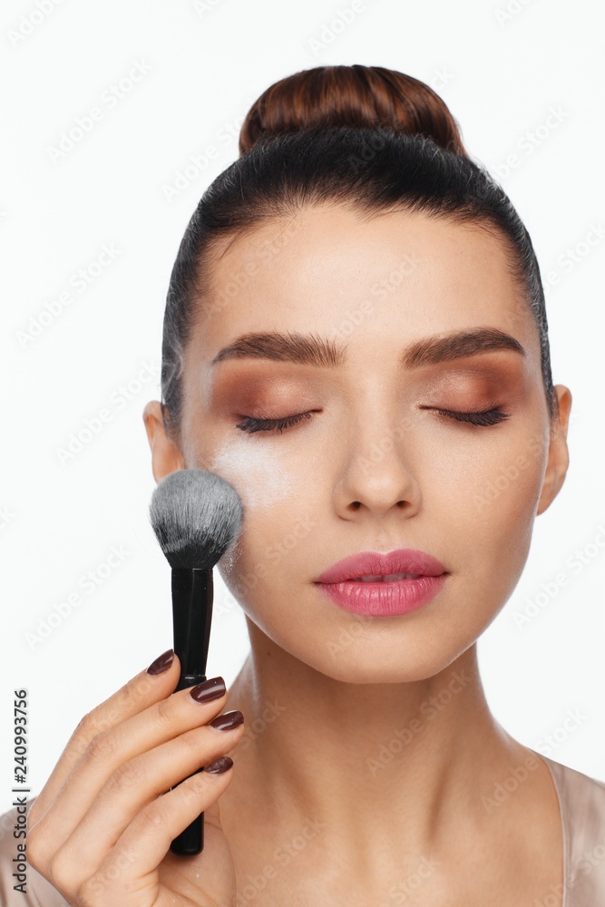 Portrait of a beautiful young woman holding a brush in her hand and applying powder to her face with a brush Portrait of a beautiful young woman holding a brush in her hand and applying powder to her face with a brush