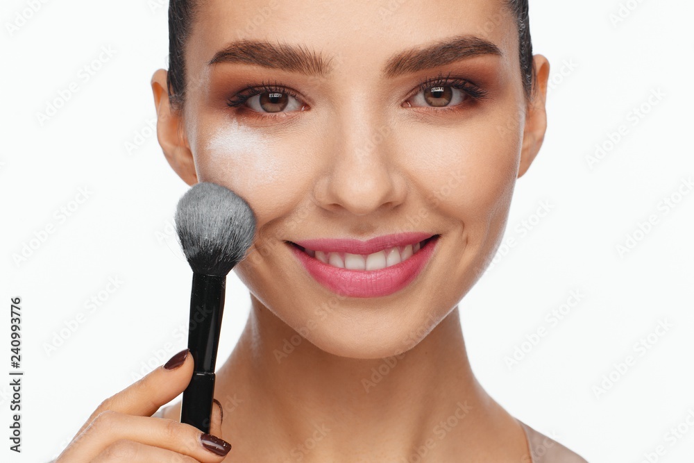© Andriy Goncharenko - Portrait of a beautiful smiling young woman holding a brush in her hand and applying powder to her face with a brush
