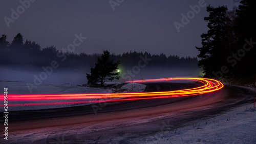 Snowy foggy forest road with car tail lights. Long exposure.