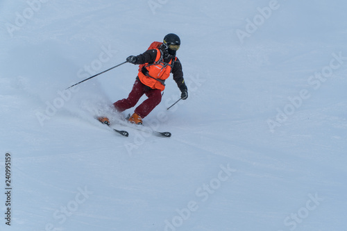 Skier skiing downhill in high mountains during sunny day.