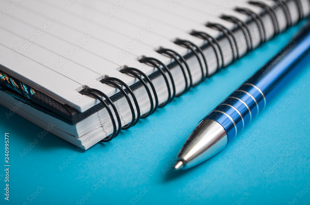closeup of blue pen on spirales notebook on blue background closeup of blue pen on spirales notebook on blue background