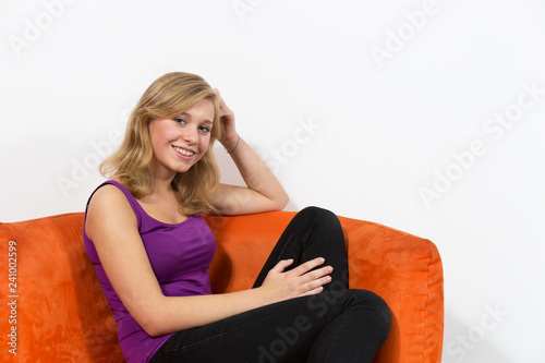 Junges Mädchen sitzt entspannt auf Couch und lacht in die Kamera