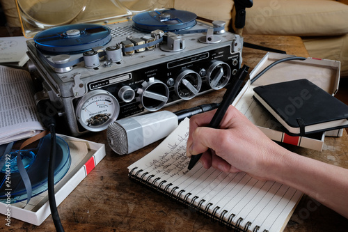 Female hand writing on notebook with tape recorder and microphone, journalist transcribing an interview, close shot photo