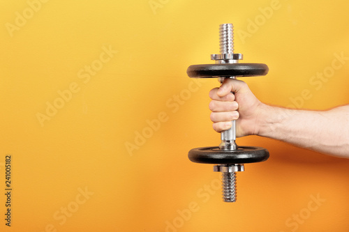 Male athlete holding metal dumbbell on color background. Space for text