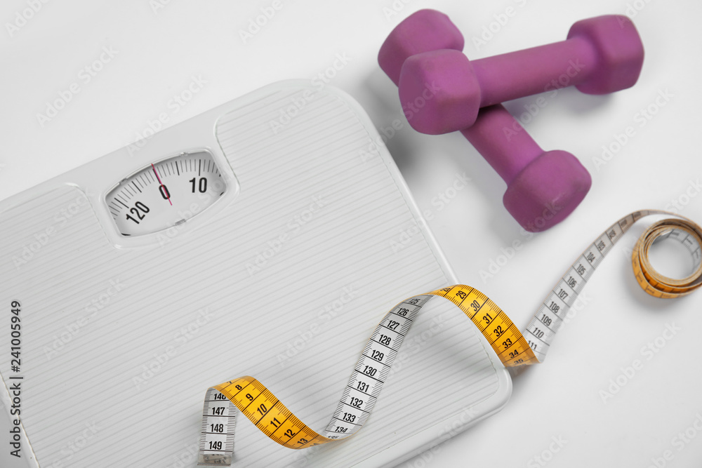 Naklejka premium Modern scales, tape measure and dumbbells on white background