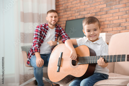 Father watching his son playing guitar at home