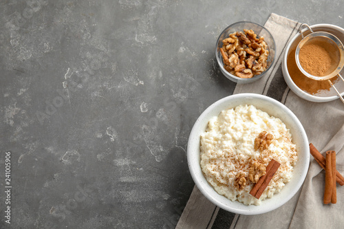 Creamy rice pudding with cinnamon and walnuts in bowl served on grey table, top view. Space for text