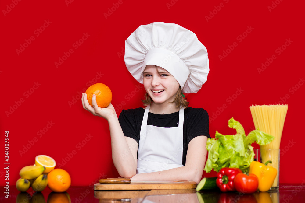 Happy little girl in chef uniform cuts fruit in kitchen. Kid chef. Cooking Concept Happy little girl in chef uniform cuts fruit in kitchen. Kid chef. Cooking Concept