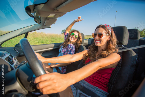 Two young beautiful girls driving in a convertible