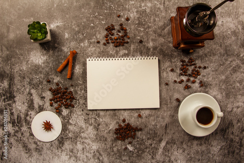 Template mockup clean notebook with cup of coffee, coffee grains, cinnamon, coffee grinder on gray background. View from above. Layout of ideas.