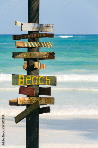 A signpost with Beach written on it with tropical beach and ocean in background on a sunny afternoon