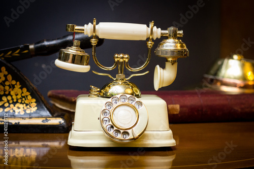 An old gold plated telephone with a rotary dial on an antique table in the foyer of Zimbabwe's oldest hotel, Meikles Hotel. Old guest books, a paper guillotine in the background. (ID: 241028712)