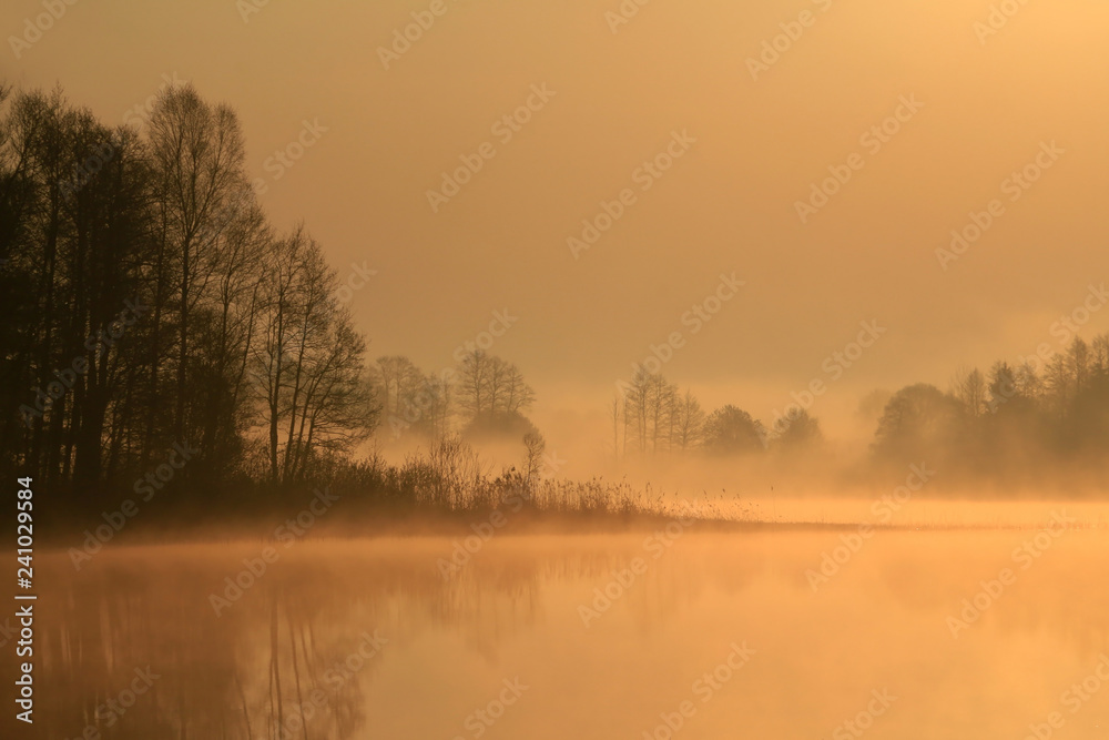 Beautiful gentle orange sunrise over the lake in a misty morning.