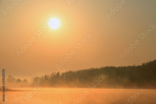 Beautiful gentle orange sunrise over the lake in a misty morning.