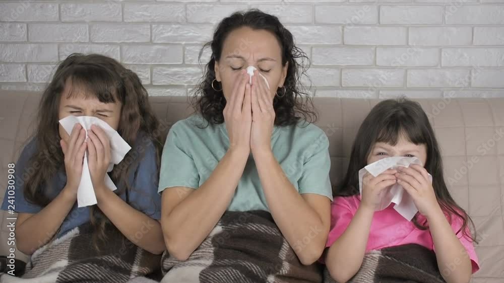 Family with a cold. Mother with daughters with a runny nose. Sick woman with children pee and wipe their nose with handkerchiefs. Family with a cold. Mother with daughters with a runny nose. Sick woman with children pee and wipe their nose with handkerchiefs.