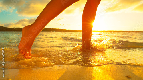LENS FLARE: Girl splashes the glassy sea water as she runs along sandy shore.