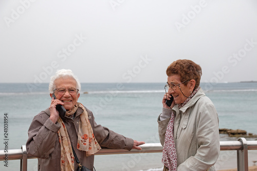 Two old women talking with a cellphone and smiling.