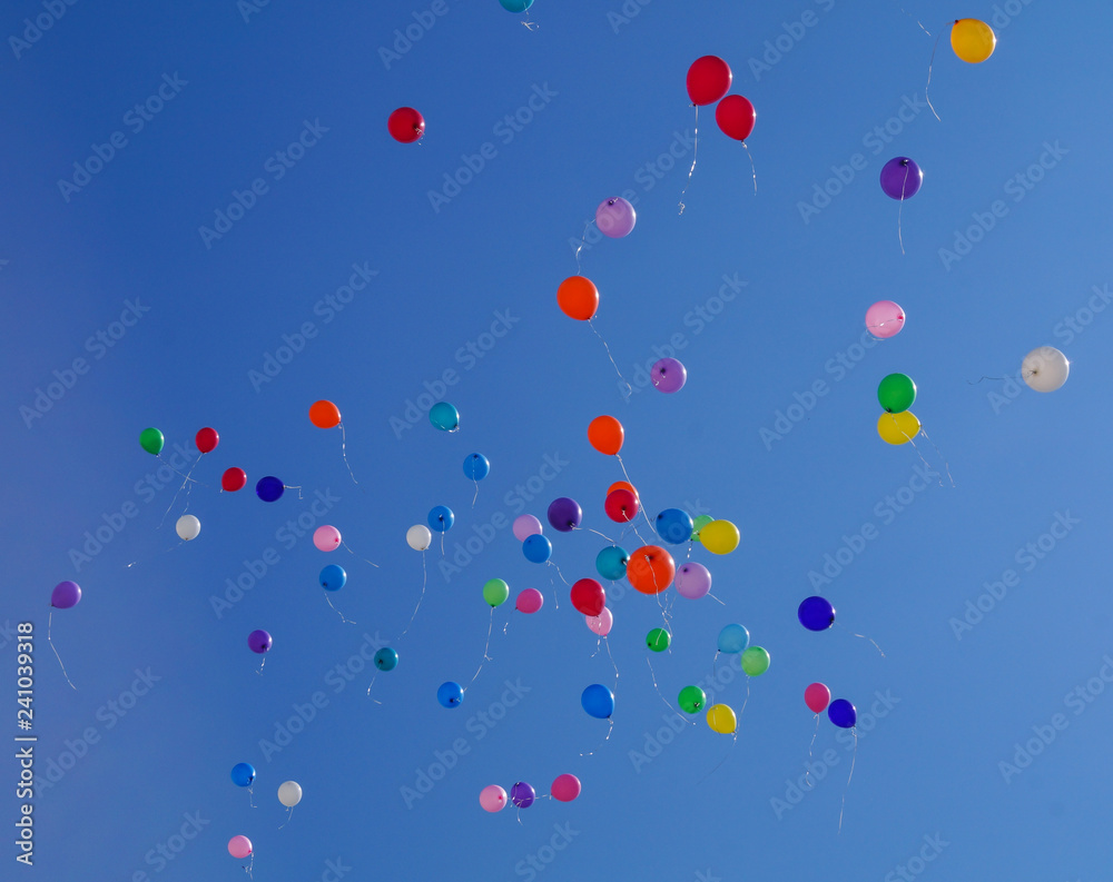 Colorful multicolored inflatable balls fly in air against background blue sky during festive festival