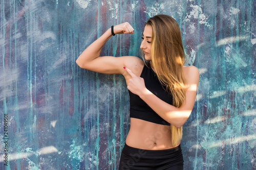 Young fitness sport woman in sportwear showing biceps outdoors on urban background