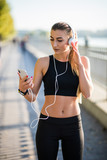 Beautiful fit and healthy woman road running while listening to music on her phone in the summer street