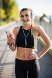 Beautiful futness woman running on street, listening music. Beautiful girl runner with Sports devices : Fitness Tracker, Headphones And Armband Jogging Outdoors.