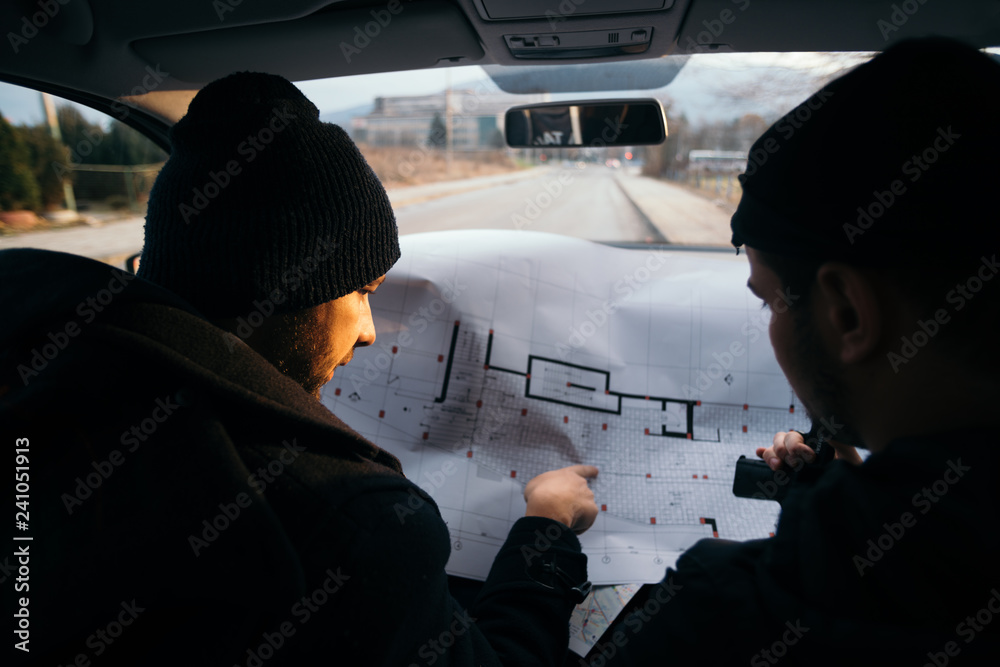 Two robbers planning and pointing on the blueprint(map) their objective while holding their guns.