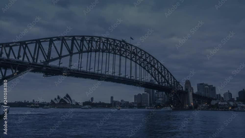 Day to night timelapse transition in Sydney, Australia with the majestic Sydney Harbour Bridge and illuminated cityscape of business towers in the background. Day to night timelapse transition in Sydney, Australia with the majestic Sydney Harbour Bridge and illuminated cityscape of business towers in the background.