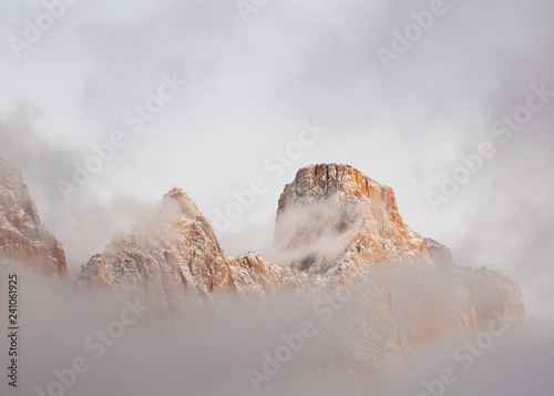 Mt. Kinesava is shrouded in clouds with the snow covered peaks breaking through in the soft light before sunrise on a December morning near Zion national park in Southern Utah.