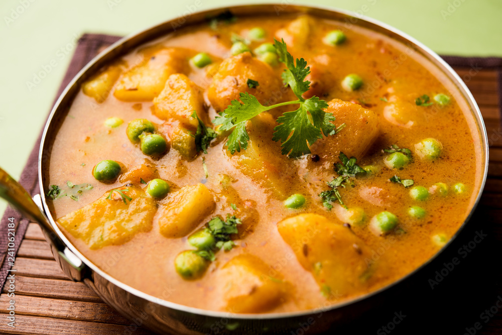 Indian Aloo Mutter curry - Potato and Peas immersed in an Onion Tomato Gravy and garnished with coriander leaves. Served in a Karahi/kadhai or pan or bowl. selective focus Indian Aloo Mutter curry - Potato and Peas immersed in an Onion Tomato Gravy and garnished with coriander leaves. Served in a Karahi/kadhai or pan or bowl. selective focus