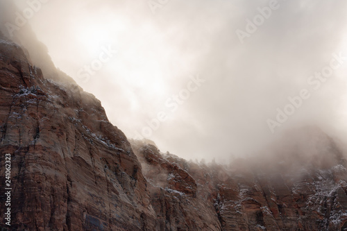 Winter storm clouds drift over the snow laced towering red sandstone cliffs of Zion national park.