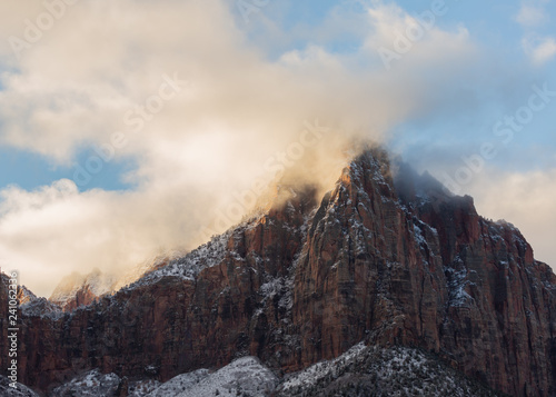 Morning sunlight begins to burn away the clouds that drift across this mountain peak after a winter snow storm in Zion national park Utah.