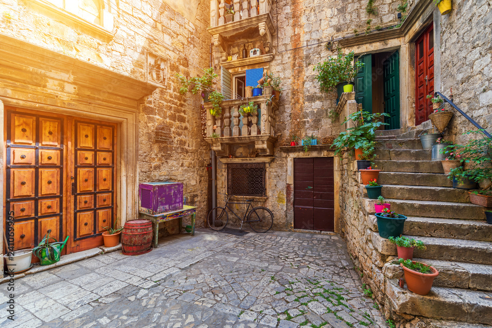 Naklejka premium Wąska ulica w zabytkowym mieście Trogir, Chorwacja. Cel podróży. Wąska stara ulica w mieście Trogir, Chorwacja. Aleje starego miasta Trogiru są bardzo malownicze i pełne uroku. Chorwacja.