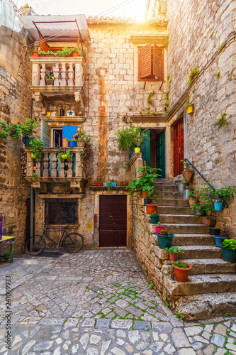 Fototapeta Naklejka Na Ścianę i Meble -  Narrow street in historic town Trogir, Croatia. Travel destination. Narrow old street in Trogir city, Croatia. The alleys of the old town of Trogir are very picturesque and full of charm. Croatia.