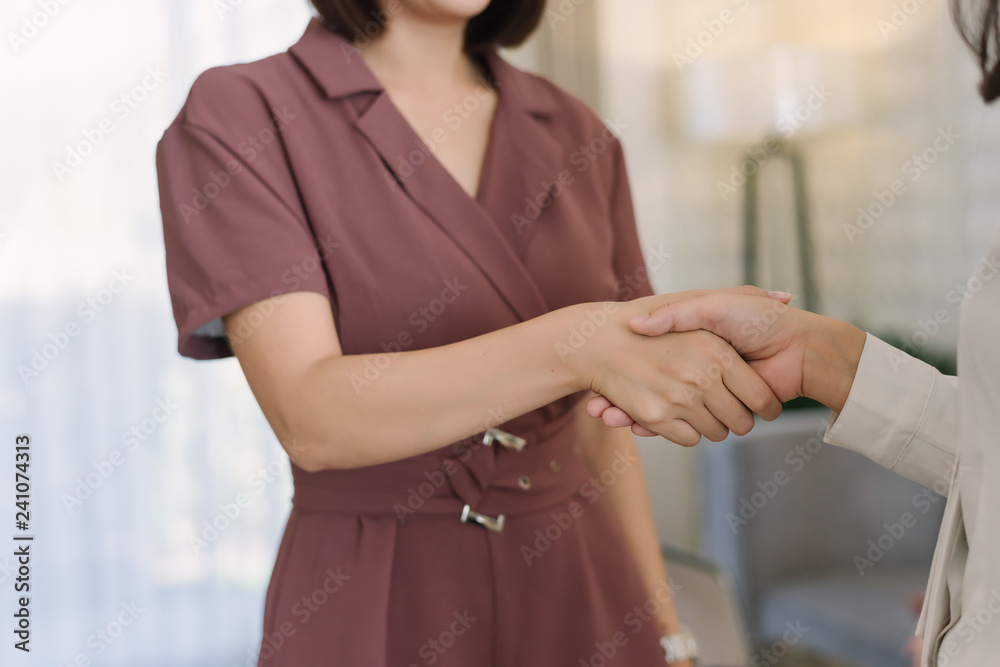 Two beautiful Asian business woman shaking hands in office during the meeting.