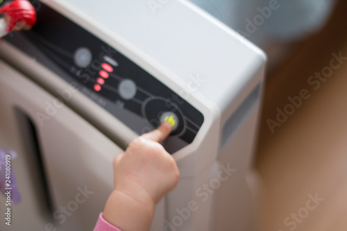 The baby's hand pressing the power button on the air purifier to clean up the polluted air.