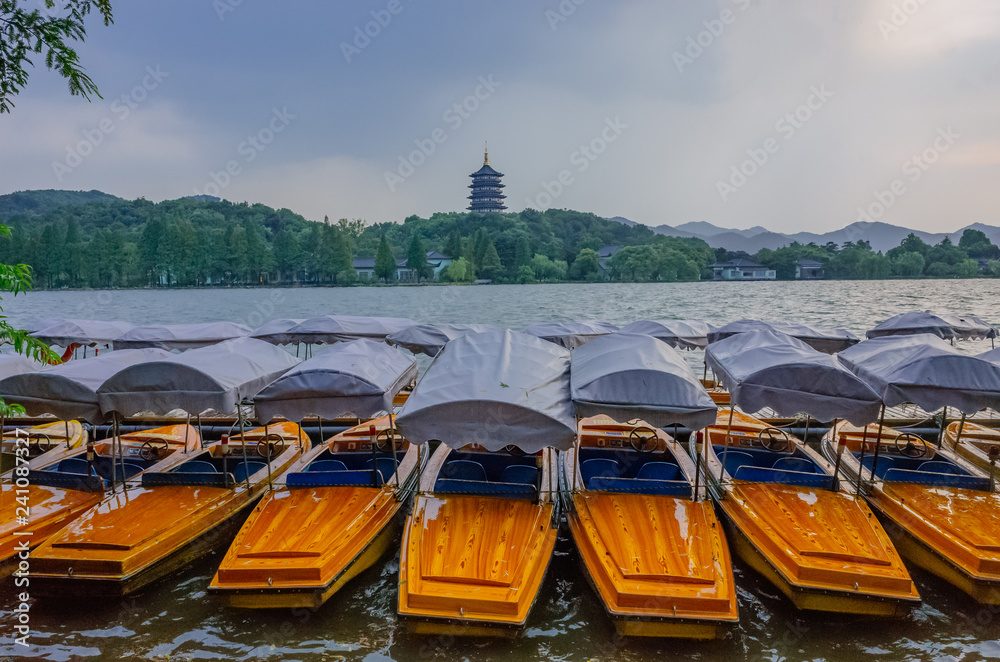 Boats docked by shore with view of the west lake and Leifeng Pagoda on hills, in Hangzhou, China