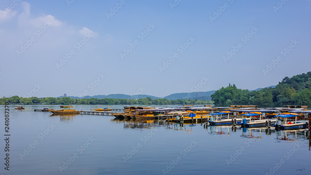 Boats at dock over calm water of West Lake, with hills in distance, in Hangzhou, China