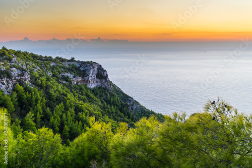 Greece, Zakynthos, Impressive orange glowing sky behind green cliff and endless blue ocean