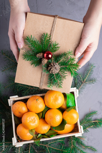 hands holding christmas gift and oranges in woden box