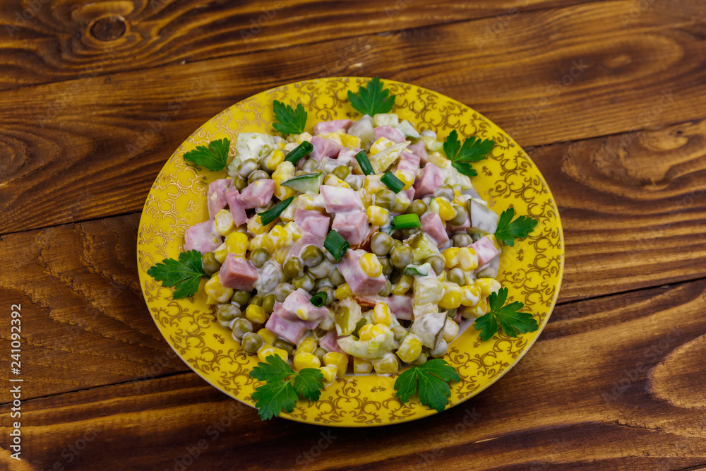 Tasty salad with sausage, green pea, canned corn, bell pepper, cucumber and mayonnaise on wooden table