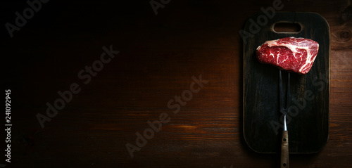 a piece of fresh marbled beef on a wooden background, with spices for cooking steak
