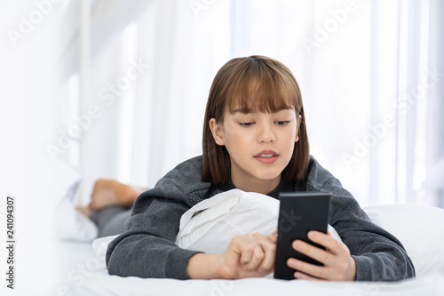 Beautiful Attractive Asian woman lying on white bed using smartphone using social media in bedroom smile and happiness with social media and shopping online,Lifestyle in Holidays Concept
