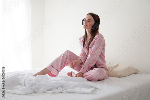 woman in pink Pajamas listening to music in headphones dancing on the bed