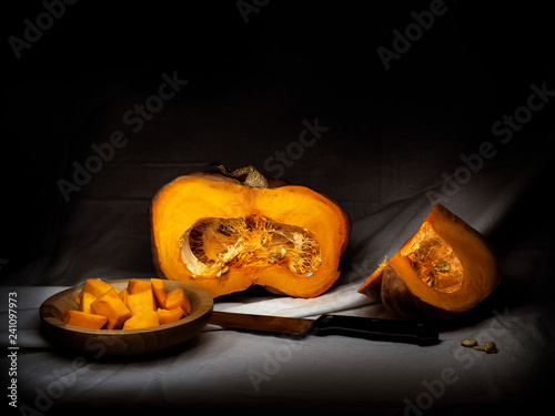 Acorn winter squash, pumpkin, prepared for cooking, cubes with seeds, knife. Chiaroscuro, baroque style light painting. photo