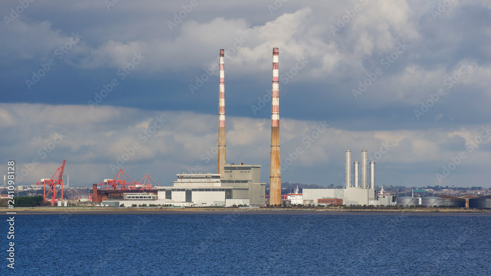 Flue-gas stacks/chimneys of a decommissioned waste incinerator  next to the buildings of a new Waste to Energy Facility. Industrial landscape on the Poolbeg peninsula in Dublin, Ireland.