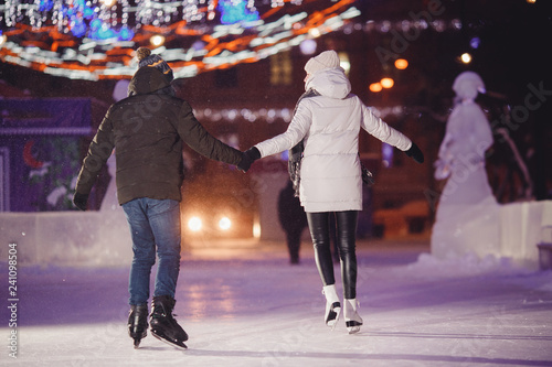 Winter skates, loving couple holding hands and rolling on rink. Illumination in background, night. Concept training. Back view