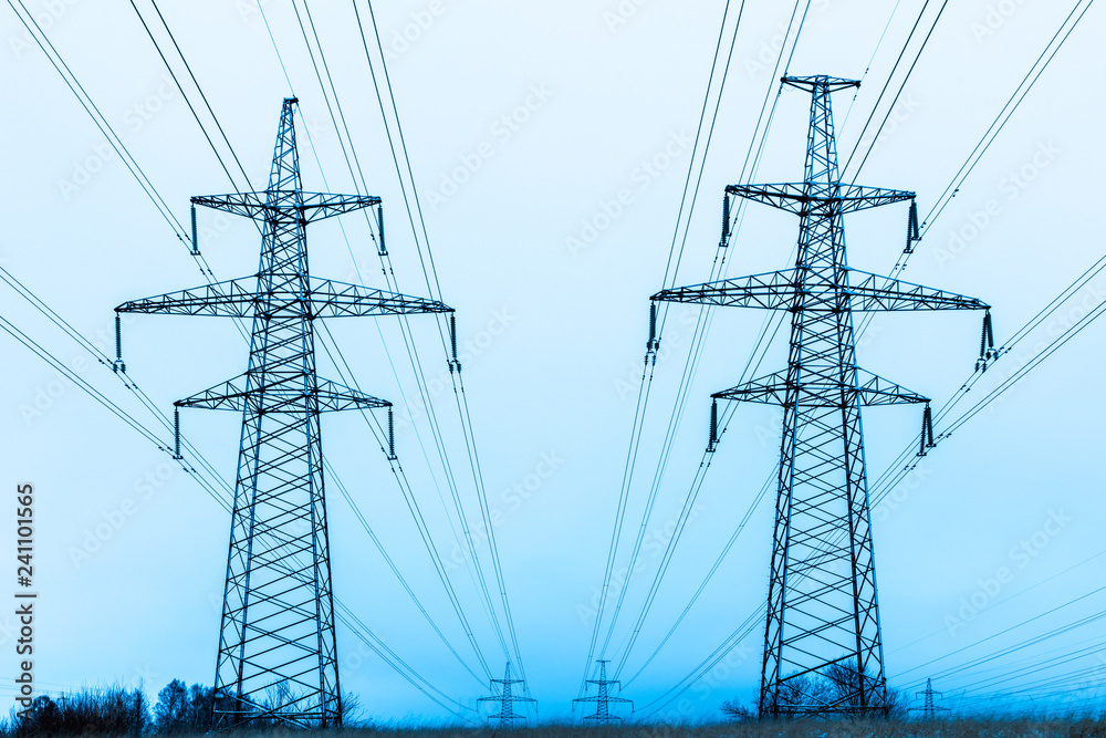Towers of electric main in the winter snowy countryside field on the background of blue sky and the forest with the wires Towers of electric main in the winter snowy countryside field on the background of blue sky and the forest with the wires