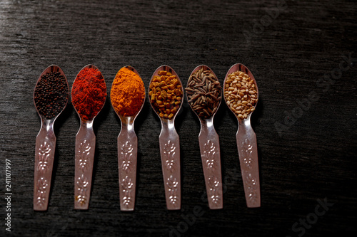 spices in spoons on black background