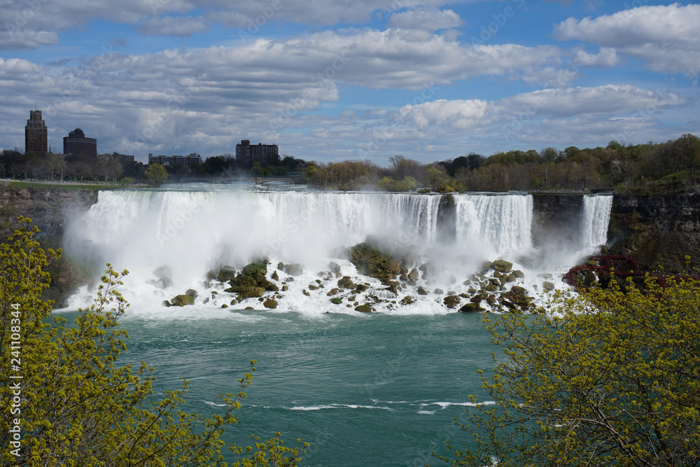 Niagara Falls waterfall on bright spring day with clouds and blue sky as seen from Ontario, Canada