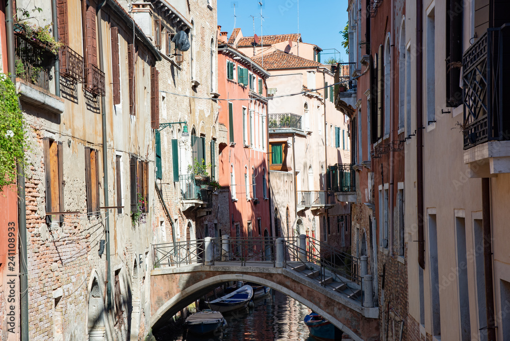 Typical Venetian buildings with canal and bridge in Venice, Italy. Old houses along the banks of water with boats.